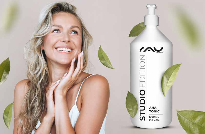 Frau mit langem blonden Haar lächelt neben der AHA Tonic Flasche, STUDIO EDITION, von RAU Cosmetics.