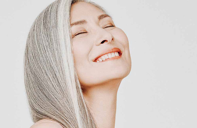 Der Anti-Aging Geheimtipp aus Asien - weißer Tee! Lächelnde Frau mit grauen Haaren und strahlender Haut, repräsentiert die Anti-Aging-Vorteile von Hautpflegeprodukten mit weißem Tee.